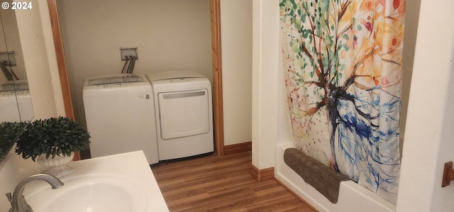 clothes washing area featuring wood-type flooring, separate washer and dryer, and sink