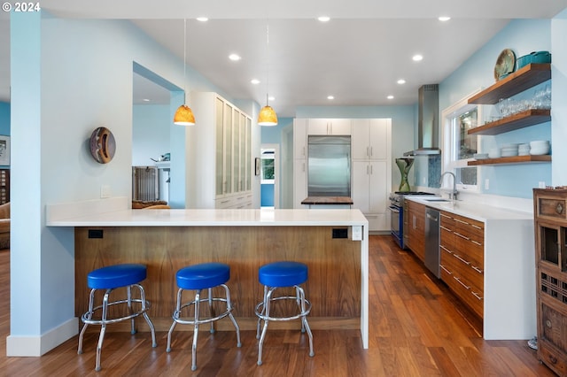 kitchen with white cabinetry, appliances with stainless steel finishes, a kitchen breakfast bar, dark wood-type flooring, and wall chimney exhaust hood