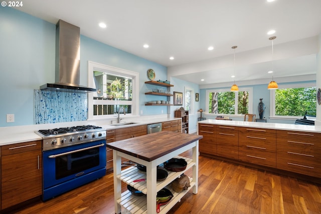 kitchen with stainless steel appliances, hardwood / wood-style flooring, sink, decorative light fixtures, and wall chimney range hood