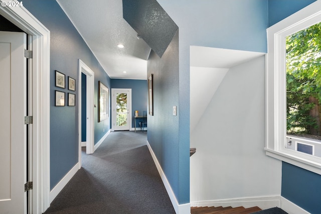 hall with dark colored carpet, plenty of natural light, and vaulted ceiling