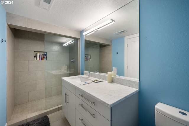 bathroom with tile patterned floors, a tile shower, vanity, a textured ceiling, and toilet