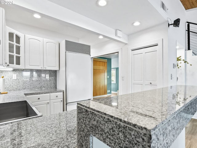 kitchen featuring light stone counters, light wood-type flooring, paneled built in refrigerator, and white cabinets