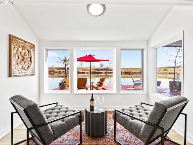 sitting room with a water view, wood-type flooring, and vaulted ceiling