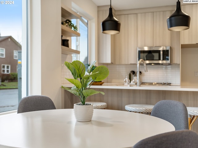 kitchen with kitchen peninsula, light brown cabinetry, decorative light fixtures, and tasteful backsplash