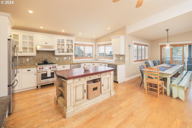 kitchen with a kitchen island, light wood-type flooring, appliances with stainless steel finishes, decorative light fixtures, and vaulted ceiling