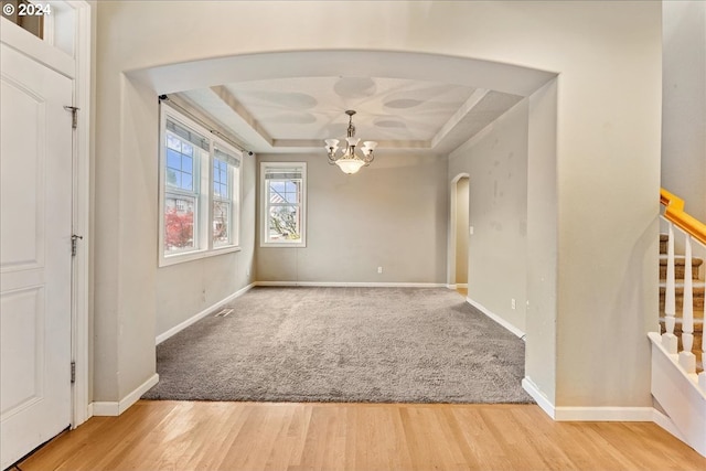 unfurnished room with a tray ceiling, a chandelier, and hardwood / wood-style flooring