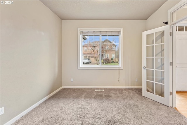 carpeted spare room with french doors and a textured ceiling