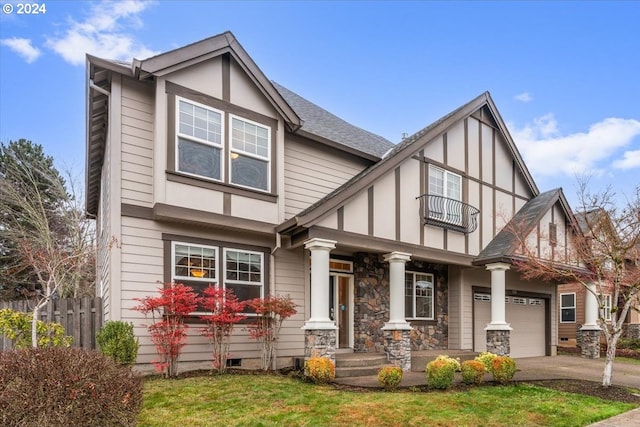 tudor home featuring a balcony, a front lawn, and a garage