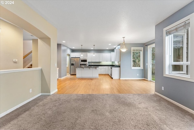 kitchen featuring pendant lighting, a center island, white cabinets, appliances with stainless steel finishes, and light hardwood / wood-style floors