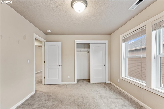 unfurnished bedroom with a textured ceiling, light carpet, and a closet