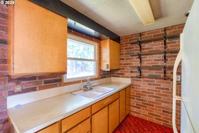 kitchen featuring sink, a textured ceiling, and brick wall