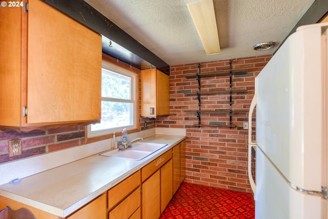 kitchen with sink, a textured ceiling, brick wall, and white fridge