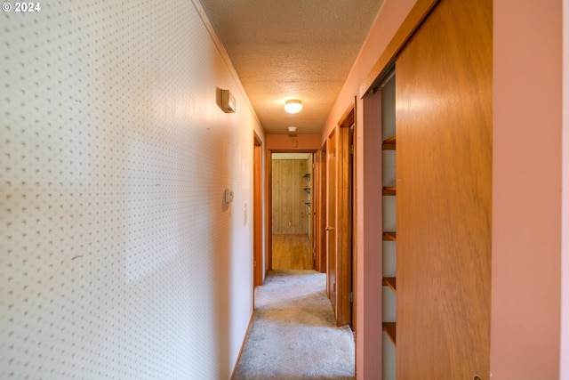 hallway featuring a textured ceiling, light colored carpet, and crown molding