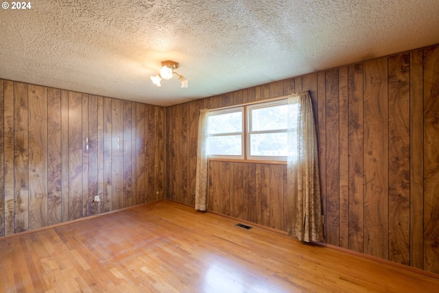 unfurnished room featuring light hardwood / wood-style floors, an inviting chandelier, wooden walls, and a textured ceiling