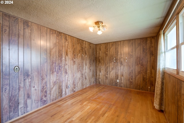 unfurnished room with a textured ceiling, wood walls, and hardwood / wood-style floors