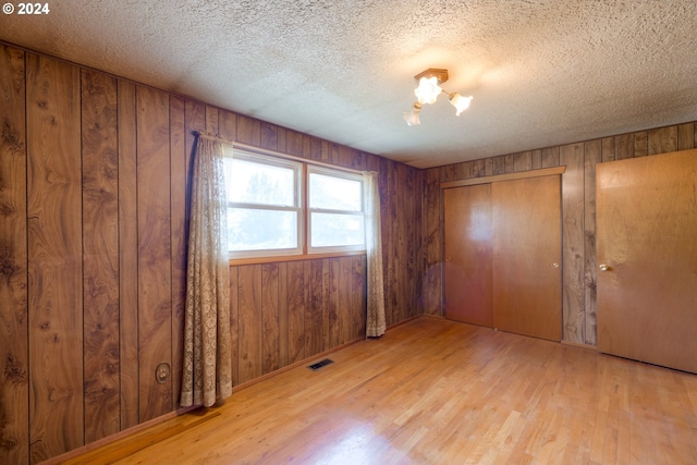 unfurnished bedroom with a textured ceiling, wooden walls, light hardwood / wood-style flooring, and an inviting chandelier