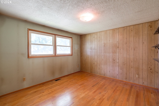 empty room with a textured ceiling, light hardwood / wood-style floors, and wooden walls