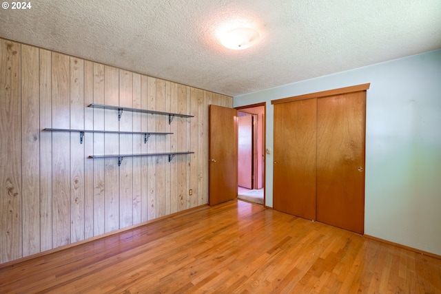 unfurnished bedroom featuring a textured ceiling, wooden walls, light hardwood / wood-style floors, and a closet