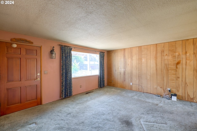 carpeted empty room with a textured ceiling and wooden walls