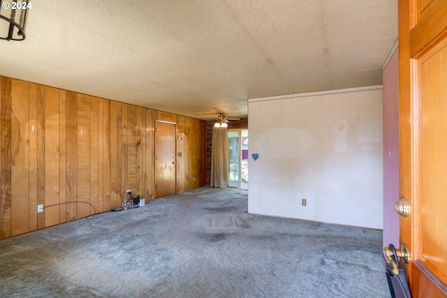 carpeted spare room with ceiling fan, wood walls, and a textured ceiling