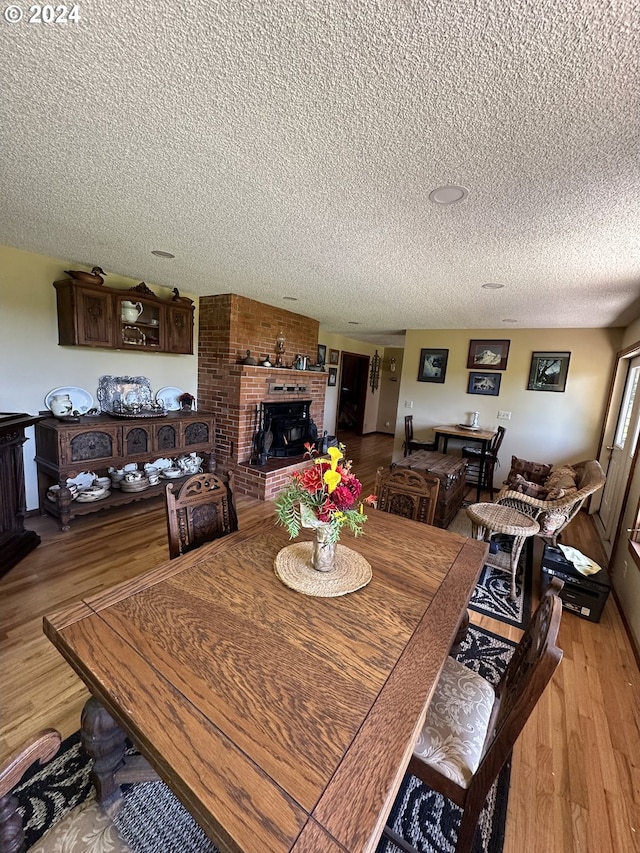 dining room featuring light hardwood / wood-style floors, brick wall, a textured ceiling, and a brick fireplace