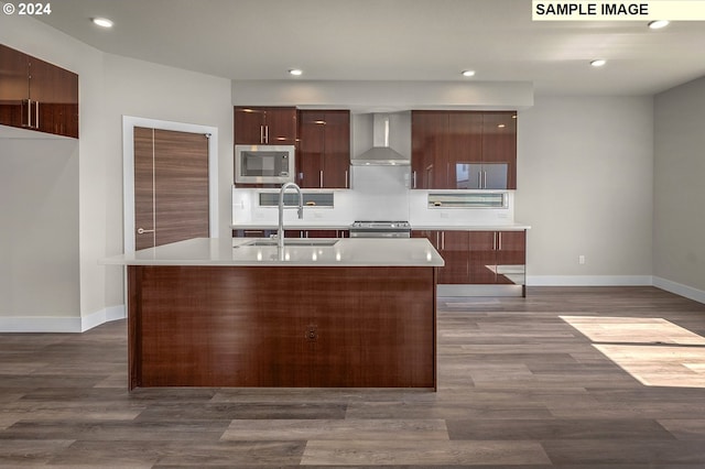 kitchen featuring appliances with stainless steel finishes, sink, wall chimney range hood, and an island with sink