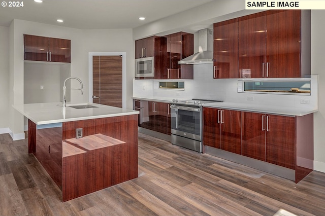 kitchen featuring wall chimney range hood, an island with sink, dark wood-type flooring, sink, and stainless steel appliances