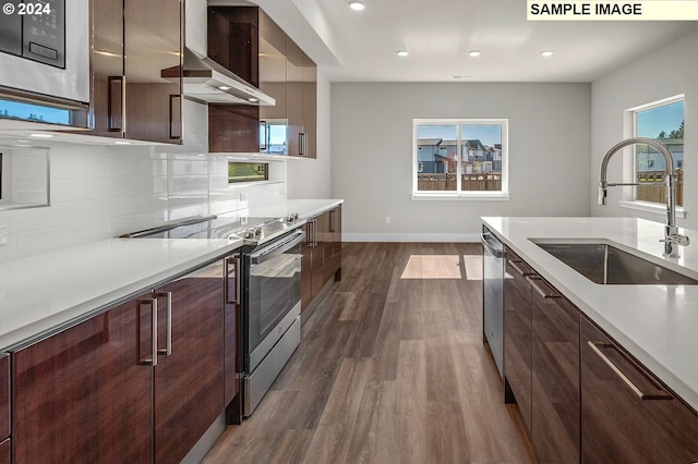 kitchen with wall chimney range hood, decorative backsplash, appliances with stainless steel finishes, dark hardwood / wood-style floors, and sink