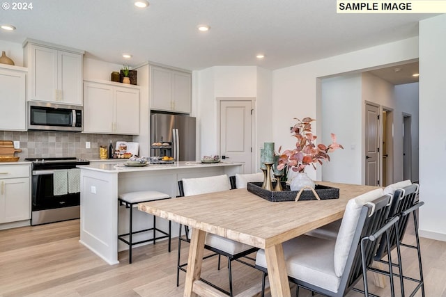 kitchen with a kitchen island with sink, light wood-type flooring, a kitchen bar, white cabinetry, and stainless steel appliances