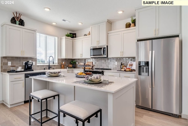 kitchen with a kitchen island, a kitchen breakfast bar, light hardwood / wood-style floors, white cabinets, and appliances with stainless steel finishes