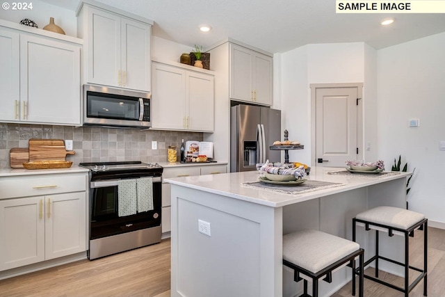 kitchen with light wood-style flooring, a kitchen island, appliances with stainless steel finishes, a kitchen bar, and backsplash