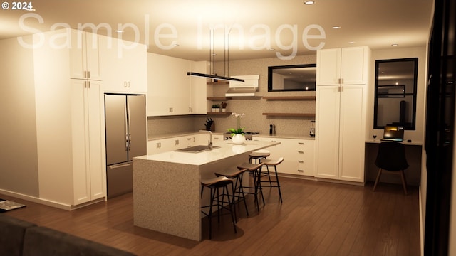 kitchen featuring a breakfast bar, dark wood-type flooring, a center island with sink, white cabinetry, and stainless steel refrigerator