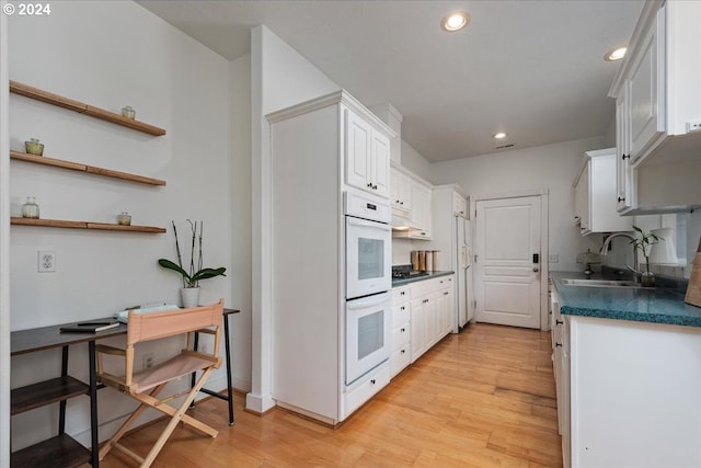 kitchen featuring white double oven, stainless steel gas cooktop, sink, light hardwood / wood-style flooring, and white cabinets