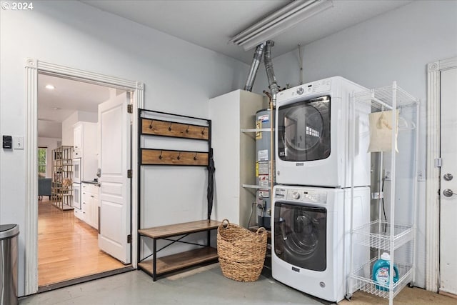 clothes washing area with strapped water heater and stacked washer and clothes dryer