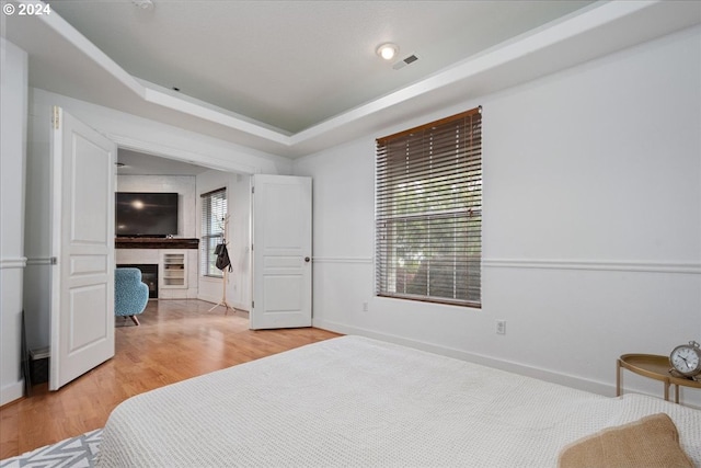 bedroom featuring light wood-type flooring, a fireplace, and a tray ceiling