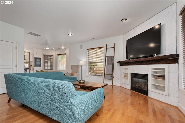 living room featuring ceiling fan, a large fireplace, and light hardwood / wood-style flooring