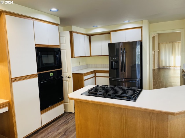 kitchen with kitchen peninsula, white cabinetry, black appliances, and hardwood / wood-style flooring