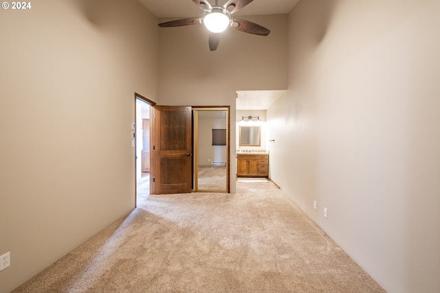 unfurnished bedroom with light carpet, ensuite bath, ceiling fan, and a towering ceiling