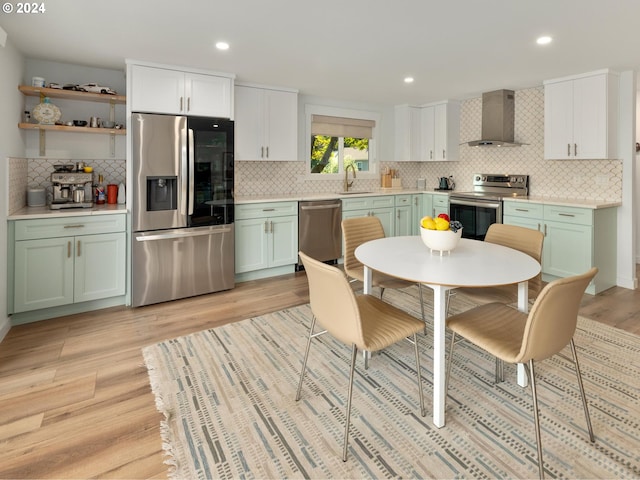 kitchen featuring backsplash, green cabinetry, stainless steel appliances, light hardwood / wood-style flooring, and wall chimney range hood