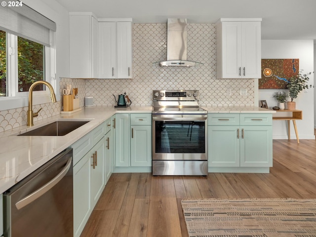 kitchen with sink, light hardwood / wood-style flooring, wall chimney range hood, appliances with stainless steel finishes, and decorative backsplash