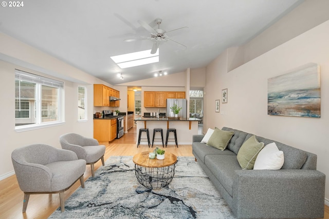 living room with vaulted ceiling with skylight and light wood-type flooring