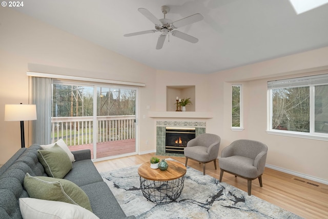 living room with lofted ceiling, wood-type flooring, a tile fireplace, and ceiling fan