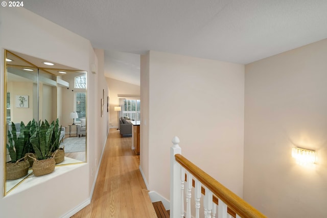 hall with light hardwood / wood-style flooring, a textured ceiling, and vaulted ceiling