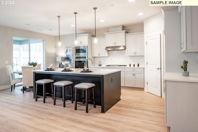 kitchen featuring decorative light fixtures, stainless steel appliances, light hardwood / wood-style floors, a center island with sink, and white cabinets