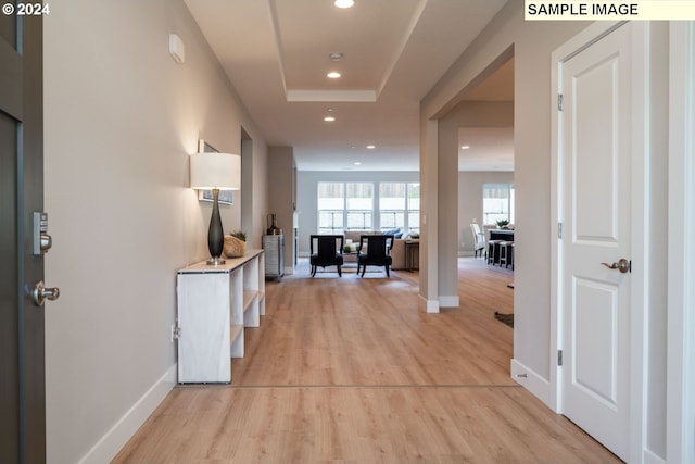 hall with a tray ceiling and light wood-type flooring