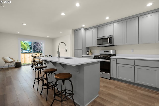 kitchen featuring an island with sink, light hardwood / wood-style flooring, sink, gray cabinetry, and stainless steel appliances