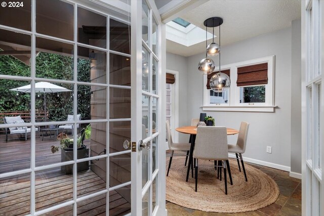 dining space with french doors, a textured ceiling, a skylight, and a healthy amount of sunlight