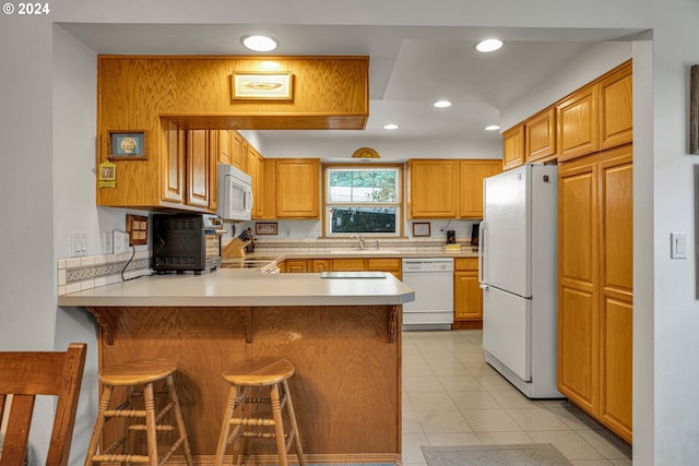 kitchen featuring light tile patterned flooring, sink, a breakfast bar area, kitchen peninsula, and white appliances