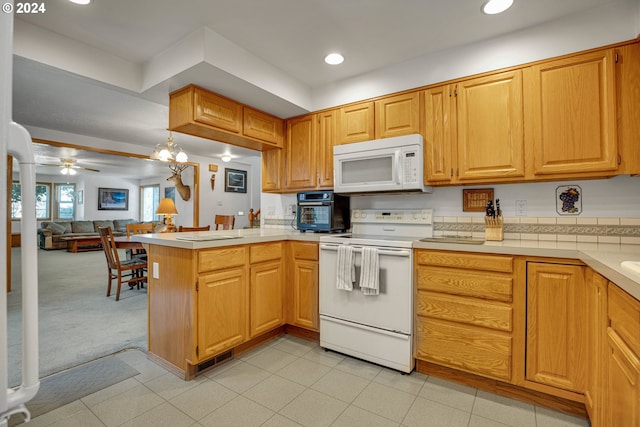 kitchen with ornate columns, ceiling fan with notable chandelier, white appliances, and kitchen peninsula