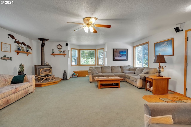 carpeted living room with ceiling fan, a textured ceiling, and a wood stove